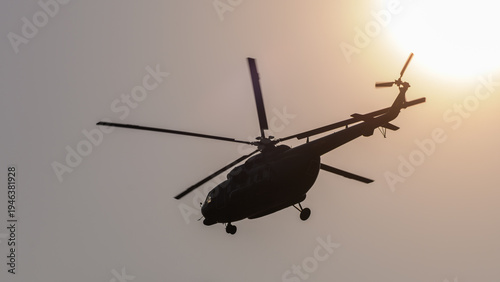 Silhouette of a helicopter flying against a glowing sun, creating a dramatic backlit aviation scene