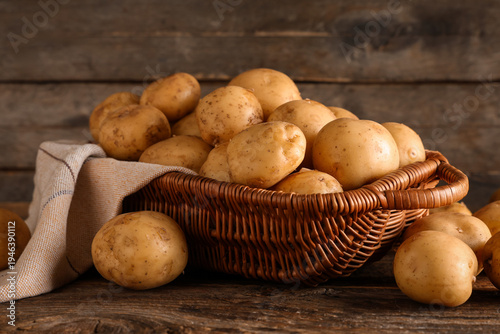 Wicker basket with raw potatoes on wooden background