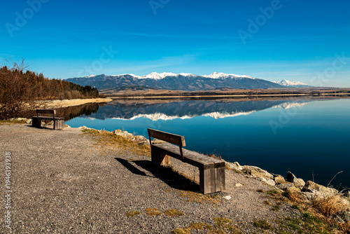 Obraz na plátne Wooden benches overlooking Liptovská Mara reservoir with reflection of the Western Tatras mountains