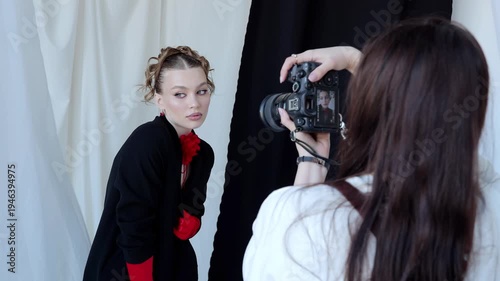 Professional photographer shooting fashion portrait of model wearing red gloves, black jacket with floral detail, posing against monochromatic studio backdrop