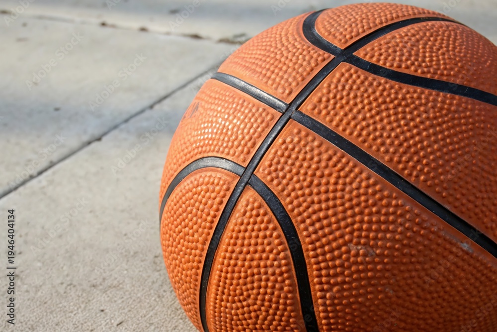 Fototapeta premium Orange basketball rests on concrete pavement