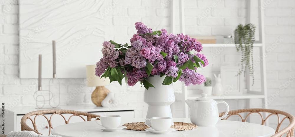 Obraz premium Vase with lilac flowers and tea set on dining table in room