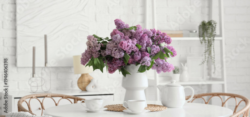 Vase with lilac flowers and tea set on dining table in room
