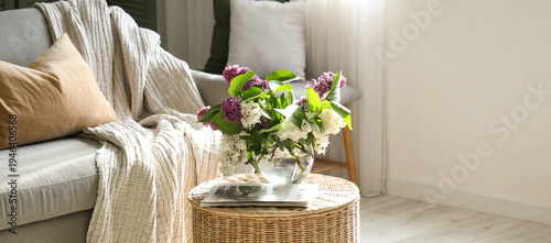 Wicker coffee table with blooming lilac branches in interior of living room
