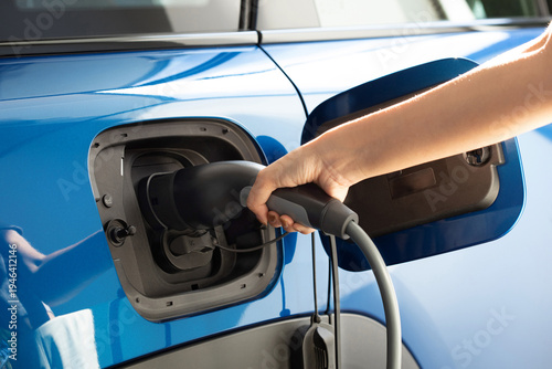 The woman is plugging in an electric vehicle charger at home.