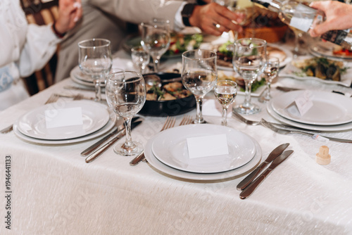 Elegant dining table set with white plates, glassware, and fine cutlery prepared for a festive celebration or formal dinner.  wedding reception, luxury restaurant, or holiday gathering.