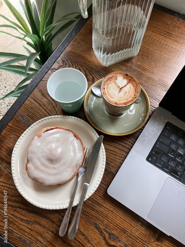 Cinnamon scroll and cappuccino with laptop at cafe 