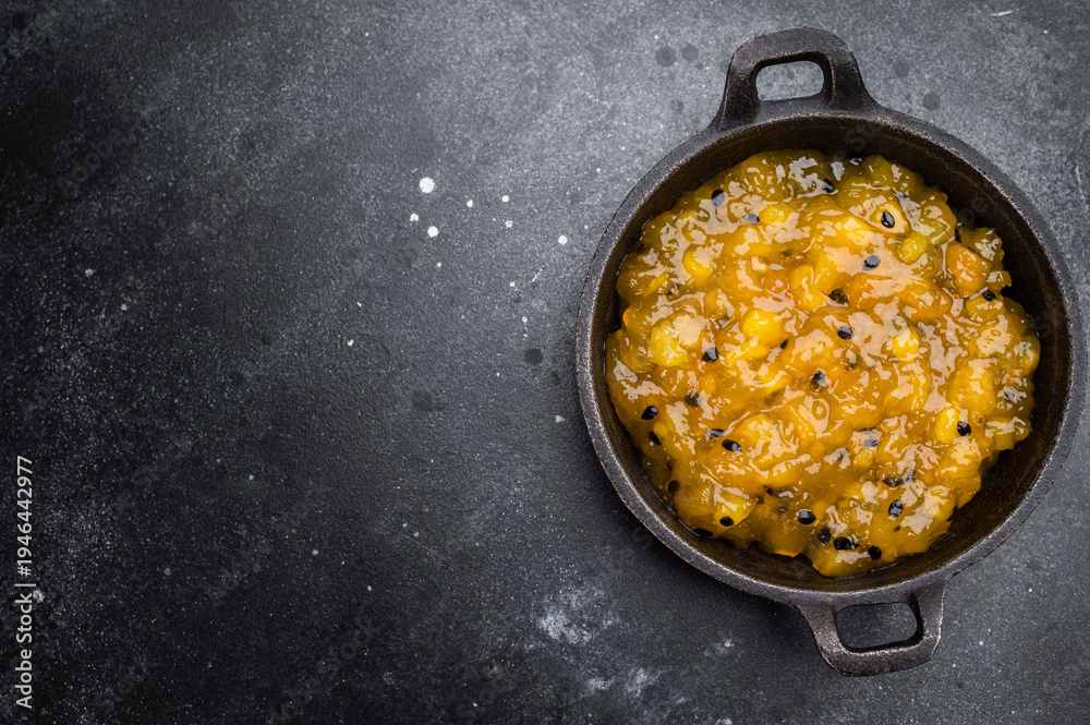 Naklejka premium Mango and passion fruit sauce in cast iron pan on dark background, gourmet tropical fruit reduction with glossy texture