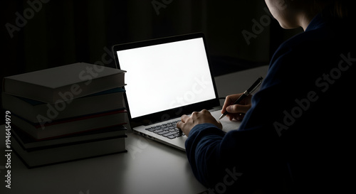 Person studying at night with laptop and books; focused student researching online with computer; dark academia lifestyle