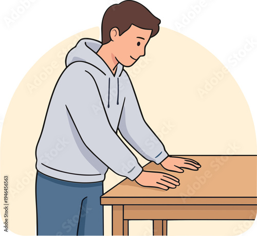 A man in a hoodie stands at a wooden table indoors.