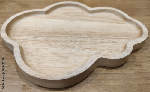 A carved wooden serving plate with decorative shape placed on a table, representing rustic restaurant tableware and antique-style food presentation