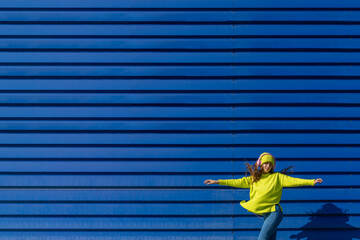 Dancing teenage girl listening music with headphones in front of blue background