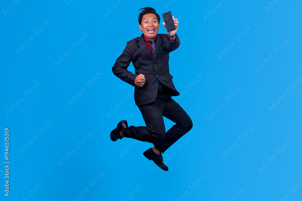 Obraz premium Full Body Shot Of Happy Asian Businessman Jumping For Joy While Holding Smartphone