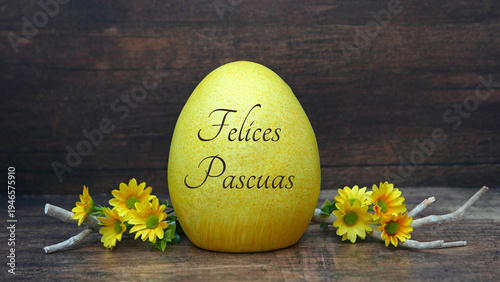 Photos Un huevo de Pascua amarillo con la inscripción Felices Pascuas sobre una mesa de madera, rodeado de flores y ramas amarillas