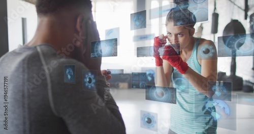 Fotografie Training female boxer wearing tank top and red hand wraps with coach in gym, hol