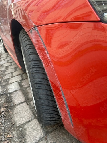 Kratzer und Lackschaden an einem roten Auto an Kotflügel und Stoßstange. Detailaufnahme eines Parkremplers, Konzept für Autoschaden, Versicherung, Reparatur und Unfall im Straßenverkehr.