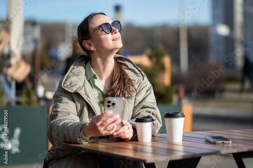 Young woman in sunglasses using smartphone at outdoor cafe table