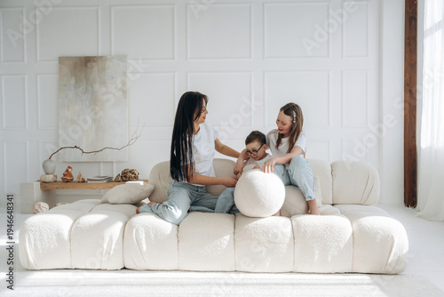 Εκτύπωση καμβά Woman and two girls play together on a modern white sofa in a bright, airy livin