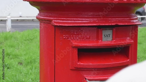 Male hand postcard into red british post box on the street. Concept of communication tradition postal service business