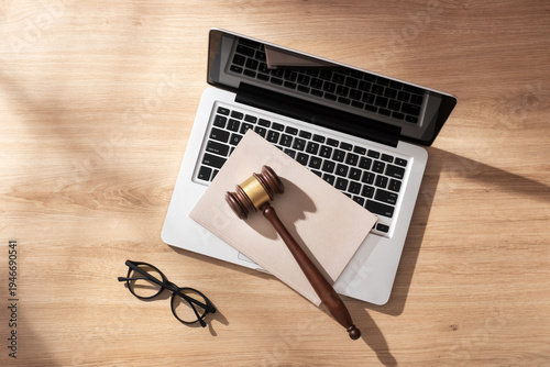 Tableau sur toile Laptop, wooden gavel with beige notebook and glasses on a light wooden desk in soft sunlight, symbolizing online auctions