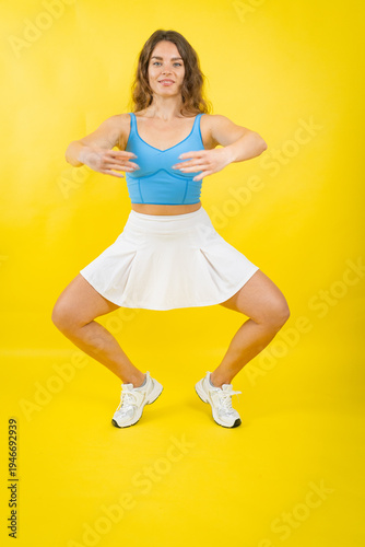 Quadro su tela Woman performing fitness exercise squatting on yellow background
