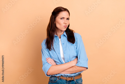 Fotografía Skeptical young woman with arms crossed wearing a blue striped shirt on beige ba