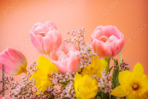 A close-up of a bright spring bouquet with soft pink tulips, bright yellow daffodils, and delicate filler flowers on a warm pastel background.