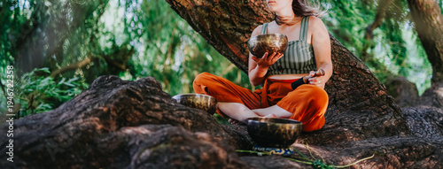 Fotografie Friends practice a sound bath with Tibetan singing bowls while seated on tree roots