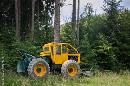 Yellow forest skidder logging tractor in green spruce forest