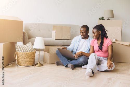 фотографія Young black couple planning their new home interiors on laptop, surrounded by mo