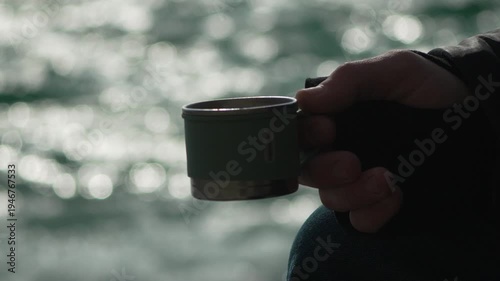 Mug steam water hand holds a steaming cup of tea outdoors by a sparkling river during a peaceful morning hike