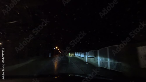 Night driving on narrow city street during rain with raindrops on windshield