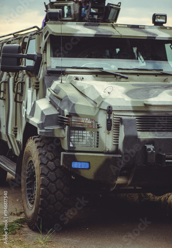 Foto A vertical close-up shot of a rugged military armored vehicle with a camouflage pattern, featuring a blue tactical light on the bumper and reinforced headlights