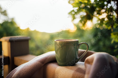 Quadro su tela Green ceramic coffee mug placed on a soft blanket on a wooden balcony railing wi