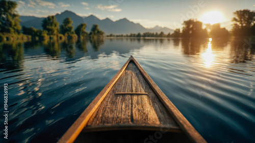 Serene view from a wooden canoe gliding on a calm lake with reflections of trees and distant mountains under a warm glowing sunset sky