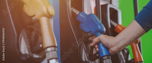 A close-up image of a gas station attendant's hand holding a fuel dispenser.	
