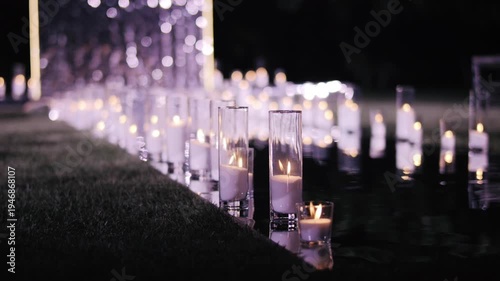 Rows of glowing candles in glass holders lighting wedding aisle at night