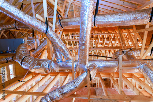 Workers install ductwork in roof of new residential building during construction