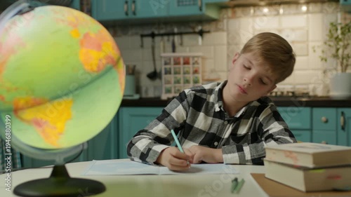 Young boy doing homework at home while looking at a globe, studying geography and learning about the world at home.