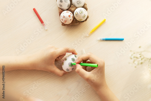 Bilde på lerret Children's hands use a green marker to color simple flower designs on white eggs