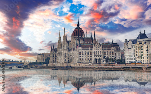 The Hungarian Parliament Building stands majestically along the banks of the Danube River under a vibrant sunset sky with its architectural details reflecting in the water.
