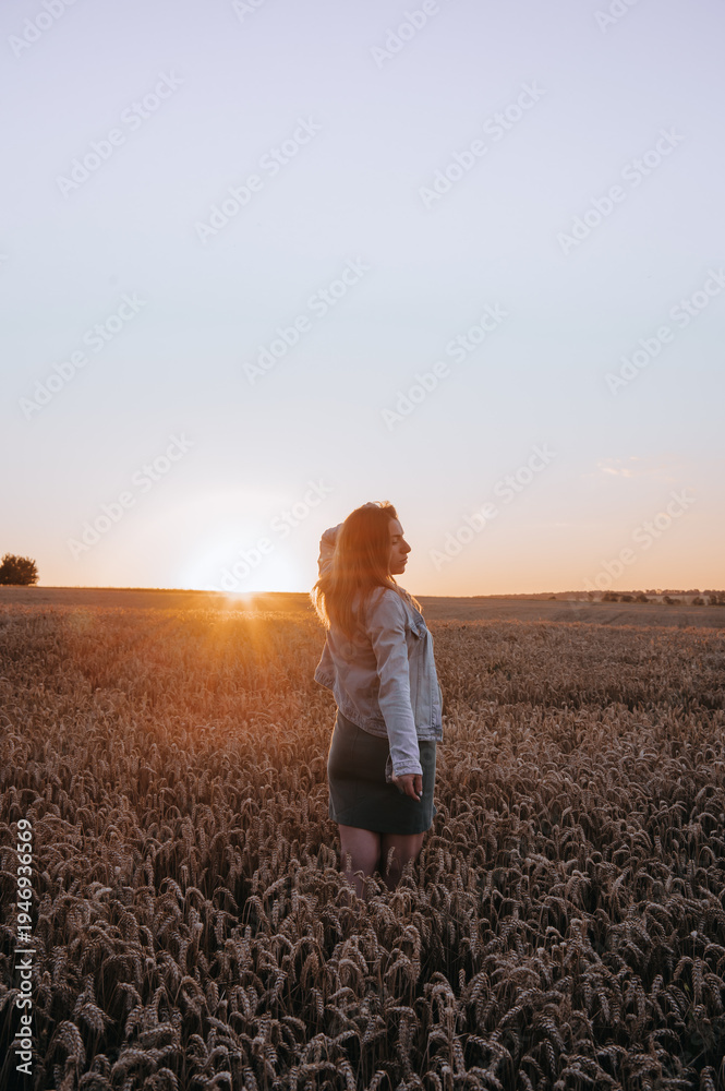 Fototapeta premium Pregnant woman holding baby socks in wheat field at sunset.