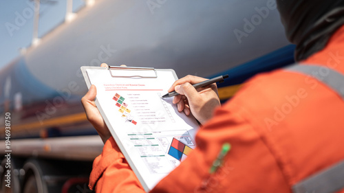 Fotografía An engineer is checking on chemical hazardous material checklist to verify the safety condition with chemical road tanker as background