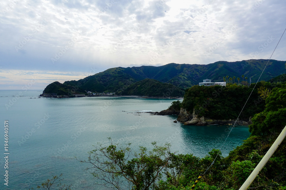 Fototapeta premium Coastal bay and forested mountains with sun rays over village on Shikoku Henro route Japan