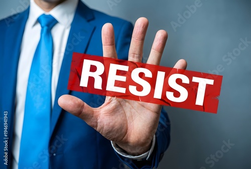 Businessman in a blue suit holding his hand up with a resist sign on a gray background