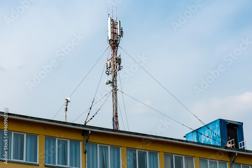 Rooftop Cell Tower Antenna on Urban Building With Guy Wires Against Blue Sky