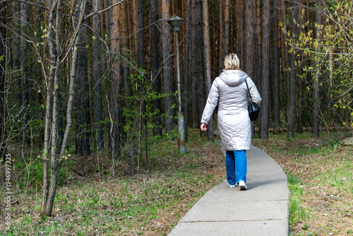 Woman Walking Alone On A Paved Path Into A Pine Forest During Early Spring