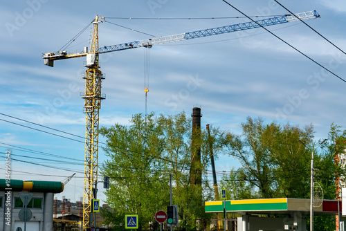 Yellow Tower Crane Over Urban Construction Site With Trees, Gas Station and Power Lines