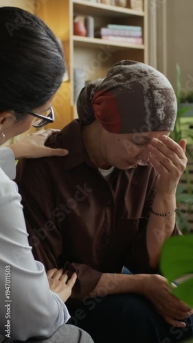 Vertical slowmo shot of mature Asian female patient wearing headscarf getting emotional and crying during counseling session in office with empathetic female psychologist gently comforting her