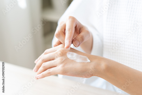 Health care, beauty asian young woman in bathrobe, towel after shower bath, spa relax at home, finger applying moisturizer on her back hand. Skin body cream moisturizing lotion, routine in morning.